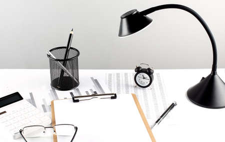Wooden clipboard ,chart and calculator, lamp and workspace accessories on a white table. copy spaceの写真素材