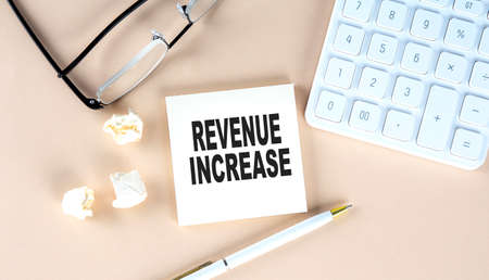 REVENUE INCREASE text on sticky with pen ,calculator and glasses on beige backgroundの写真素材