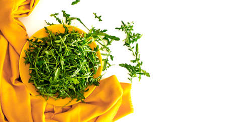 Fresh green arugula in yellow bowl on a white table with yellow towel, copy space