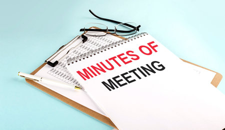 MINUTES OF THE MEETING text on a notepad on clipboard with chart on blue background, concept...
