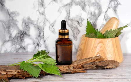 Fresh nettle in a wooden mortar. Preparation of elixirs from medicinal herbs by herbalists. The essential oil in the pharmacy bottle with pipette at cosmetologiの写真素材