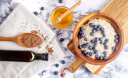 Flaxseed oil in a bottle near the seeds in a spoon. and honey and oatmeal with blueberries on wooden bowl. Health foodの写真素材