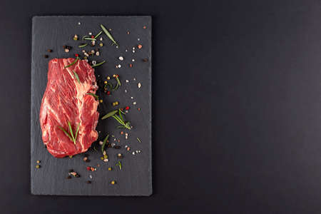 Raw steak meat with rosemary, pepper and pink salt on a dark background, copy spaceの写真素材