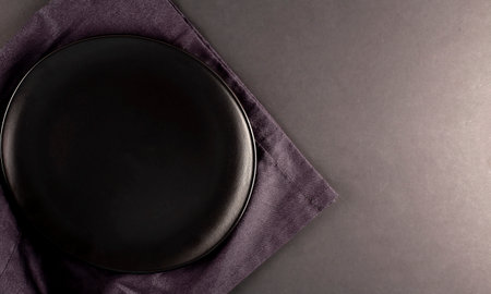 Empty round black plate on a black napkin on a dark black background, top view, copy space.の写真素材