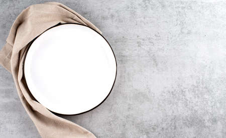 Empty ceramic plate and kitchen striped towel on light stone concrete table background. copyspace.の写真素材