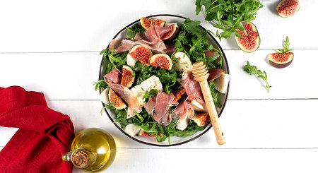 Salad with arugula , figs, prosciutto and mozzarella on a white wooden backgroundの写真素材