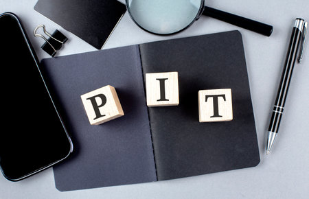 Word PIT on wooden block on a black notebook with smartpone, credit card and magnifier