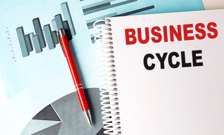 BUSINESS CYCLE text on notebook with pen on a chart backgroundの写真素材