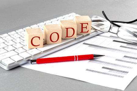 CODE written on wooden cube on the keyboard with chart on gray backgroundの写真素材