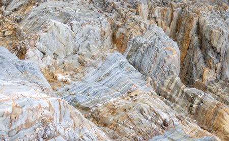 Layered rock formations featuring gray and a orange hues with intricate geological textures and...