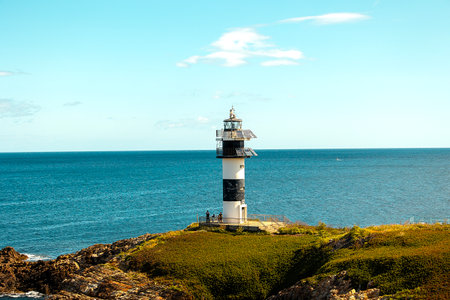 Lighthouse on a rocky coastal cliff with the blue ocean and clear sky in background.の写真素材