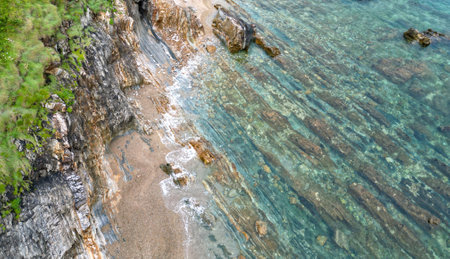 Aerial view of rocky shoreline with clear turquoise water, visible underwater rock formations, and grassy cliffsの写真素材