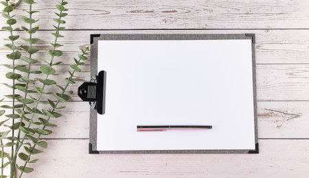 Blank paper clipboard, copy space, eucalyptus branch on a wooden background.