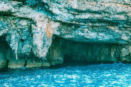 Seaside cave with rugged rocky cliffs and bright blue ocean water, creating a natural and mysterious...
