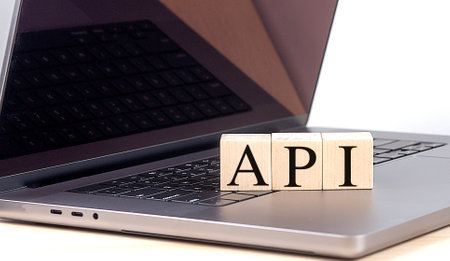 Wooden cubes with a letters api on laptop keyboard reflecting in screen .