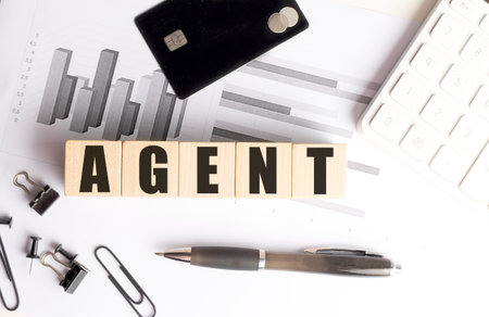 Wooden blocks with a word agent on office desk with charts, credit card, calculator and stationery...