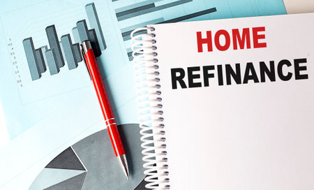 Home refinance text on a spiral notebook with red pen and financial charts on blue background. High quality photoの写真素材