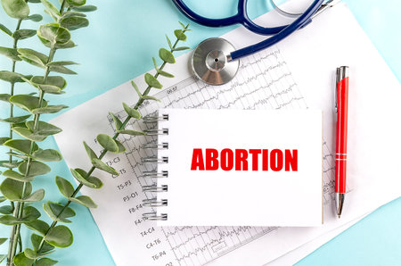 Notebook with text abortion on a medical documents with stethoscope, red pen and eucalyptus.