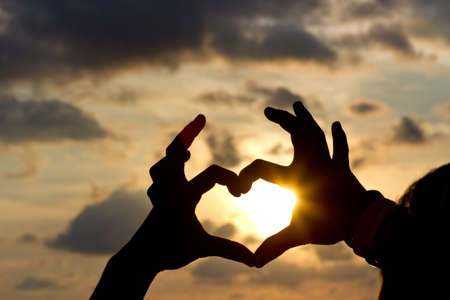 Hands in heart shape on sunset background.の写真素材
