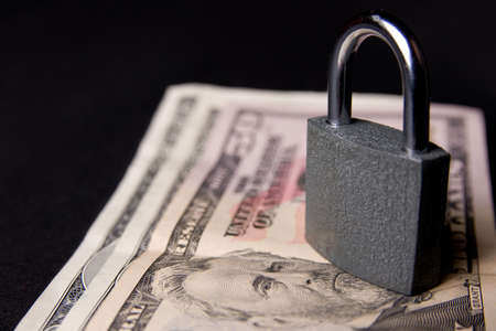 Grey closed padlock and US dollars, on dark backgroundの写真素材