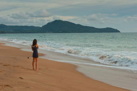 Young woman stands on the beach. Looking to the ocean waves. Evening.