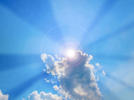 Sun beam coming out of the clouds in midday in the blue skyの写真素材
