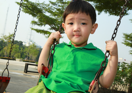 Asian boy playing swing in the parkの写真素材