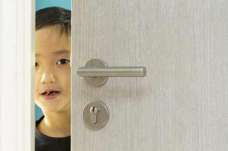 Asian boy looking out the door ajarの写真素材