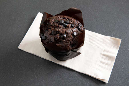 Chocolate muffin in brown paper cup with chocolate pieces on beige paperの写真素材