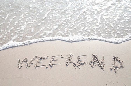 Word "WEEKEND" hand written in the sand. Close up sand texture on beach in summer. Vacation, holiday concept,の写真素材