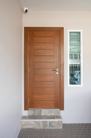 Exterior of a house with wooden door and gray tiled floor. Dark gray doormat on gray tiled floor.の写真素材