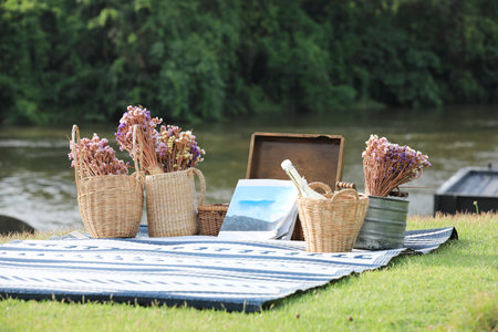 Book and flowers baskets on blue mat with river and forest in background. Vacation concept.の写真素材