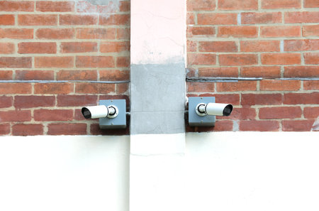 Two surveillance cameras installed on red brick wall.の写真素材