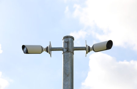 Public surveillance cameras mounted on a post with blue sky backgroundの写真素材