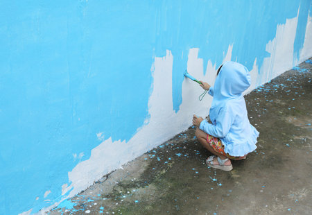 Asian girl wearing blue hooded painting blue color on old wallの写真素材