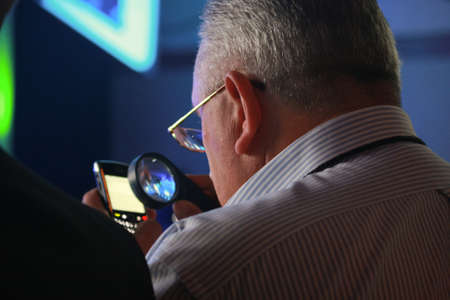 Elderly man looking at mobile phone display through loupe and glassesのeditorial素材