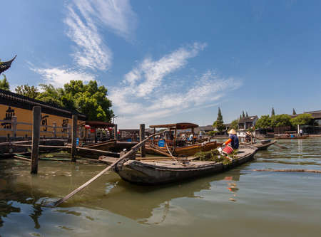 ZHUJIAJIAO, CHINA - AUGUST 30, 2016: Boatman transports underwater grass by boat made of concrete on canal of ancient water town in Zhujiajiao, China, on August 30, 2016.のeditorial素材