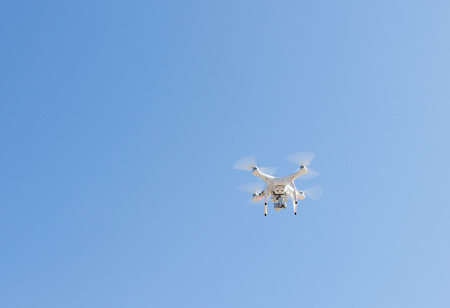 White drone, quadrocopter, with photo camera flying in the blue sky.