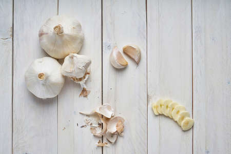 Flat lay of a still life of some heads, some cloves and slices of garlic on a white wooden tableの写真素材