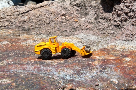 toy bulldozer with bucket on a large stone with a rough texture