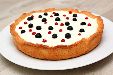 Berry tart: shortbread dough, a layer of black currant curd, whipped cream, decorated with berries of black and red currants on a white dish closeupの写真素材