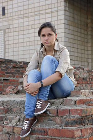 Resentful young woman sitting on the destroyed wall of the buildingの写真素材