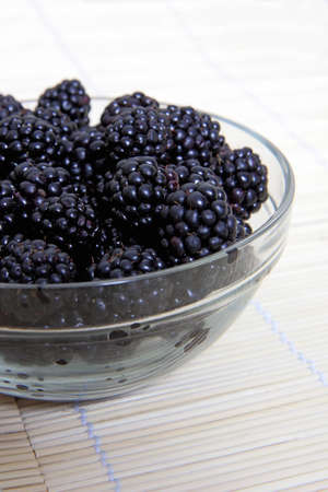Glass bowl with ripe blackberries on mat of strawの写真素材