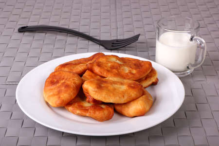 Fried cakes on white plate, fork and cup of milk on gray wicker backgroundの写真素材