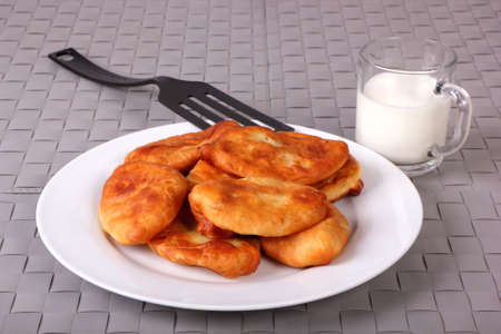 Fried cakes on white plate, plastic spatula and cup of milk on gray wicker backgroundの写真素材