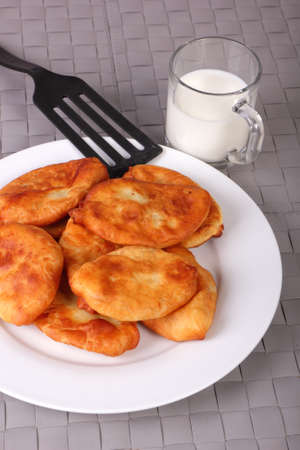 Fried cakes on white plate, plastic spatula and cup of milk on gray wicker background. Vertical photoの写真素材
