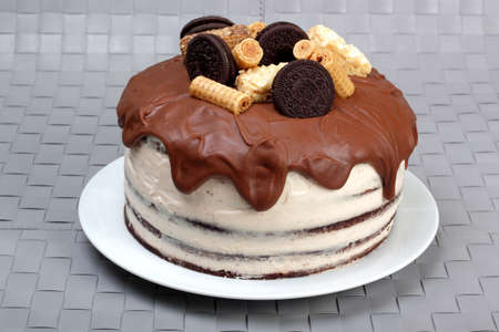 Cake, glazed with milk chocolate and decorated with waffles and cookies, on white plateの写真素材