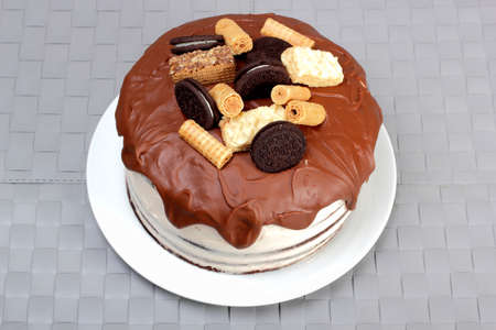 Cake, glazed with milk chocolate and decorated with waffles and cookies, on white plateの写真素材
