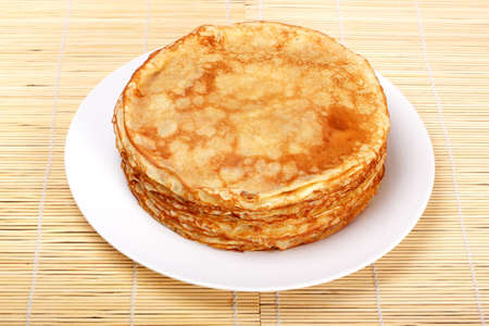 Stack of pancakes on white plate on mat of strawの写真素材