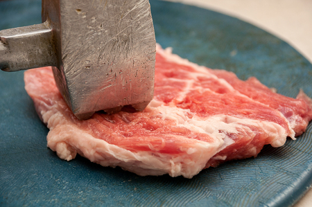 A large piece of meat fillet with fat is beaten with a heavy old aluminum mallet with notchesの写真素材